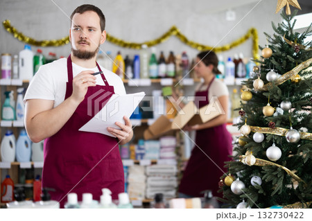Male salesperson keeps track of goods while female salesperson stocks shelves in supermarket before Christmas Male salesperson keeps track of goods while female salesperson stocks shelves in supermarket before Christmas 132730422