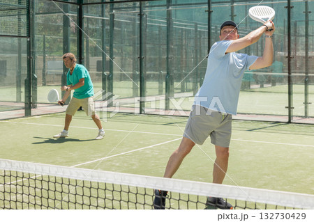 Two adult men playing doubles padel Two adult men playing doubles padel 132730429
