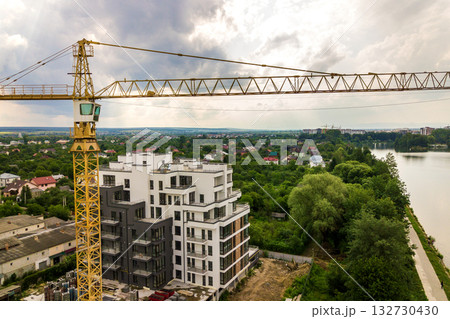 Aerial view of tower lifting crane and concrete frame of tall apartment residential building under construction in a city. Urban development and real estate growth concept. 132730430