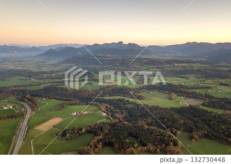 Aerial view of small scattered farm houses with red tiled roofs among green farming fields and distant mountain forest in summer. Aerial view of small scattered farm houses with red tiled roofs among green farming fields and distant mountain forest in summer. 132730448