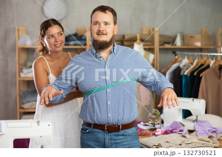 Young female dressmaker measuring male client 132730521