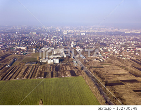 Aerial view of green and plowed fields and city suburbs on sunny dawn. Drone photography. 132730549