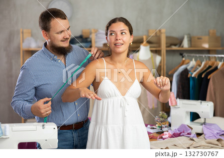 Fashion designer measuring female client for tailored clothing 132730767
