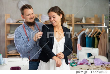 Female client trying on custom blazer with tailor in workshop 132730820
