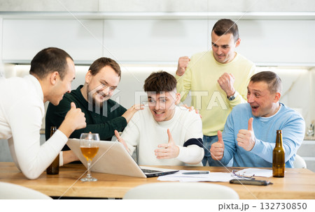 Men rejoicing over good news on laptop at home gathering Men rejoicing over good news on laptop at home gathering 132730850