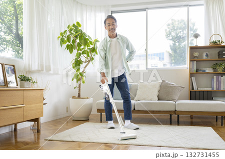 自宅リビングで掃除機をかける60代の男性　カメラ目線 132731455