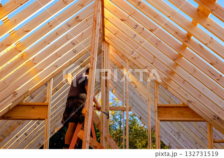 Worker constructs wooden beams frame under on roof structure of new building. 132731519