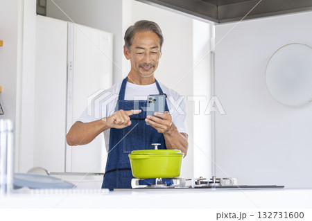 料理をしながらスマホを操作するシニア男性 料理をしながらスマホを操作するシニア男性 132731600