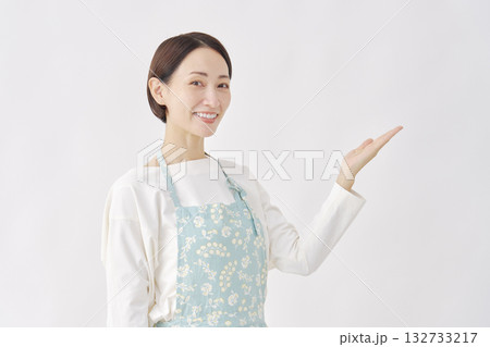 右側を手のひらで指すエプロンをつけた女性　白背景 132733217