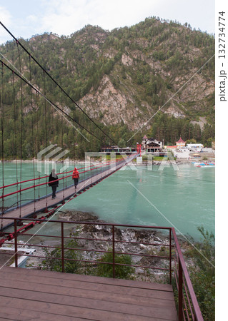 A suspension bridge spans a turquoise river, guiding travelers toward a mountain village 132734774