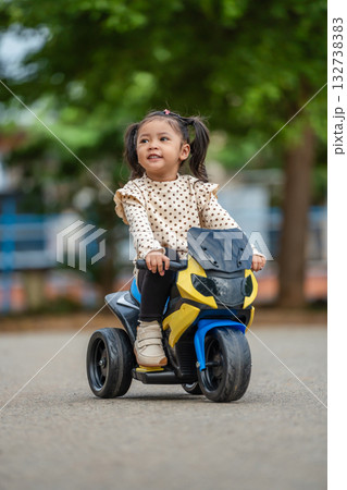 toddler girl riding an electric motorcycle toy in park toddler girl riding an electric motorcycle toy in park 132738383