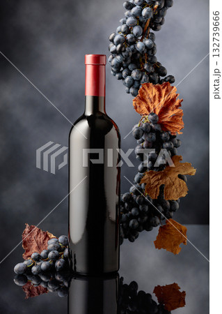 Bottle of red wine with blue grapes on a black reflective background. Bottle of red wine with blue grapes on a black reflective background. 132739666