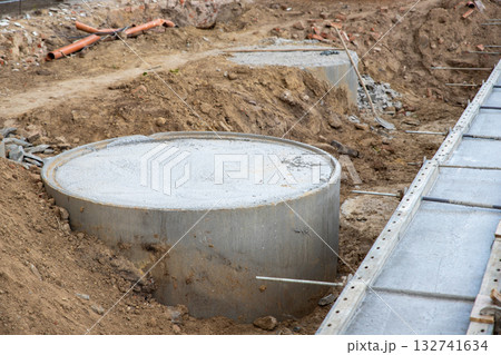 Concrete foundation poured into metal formwork at construction site. Steel rods, braces and rebar elements create strong structure supported by soil and wooden beams 132741634