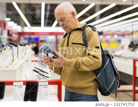 elderly grayhaired man pensioner examining counter with electronic gadgets and tablets in showroom of digital goods store 132741752