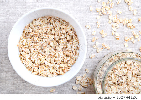 Rolled oats, thick-rolled and old-fashioned oats, in a white bowl, on linen. Dehusked and steamed oat groats, rolled into flakes under heavy rollers, then stabilized by being lightly toasted. Photo 132744126