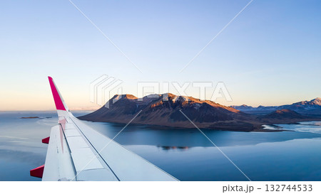 View the airplane wing in clouds with an ocean and land during a flight in the sky. Nature, horizon, travel background, or wallpaper 132744533