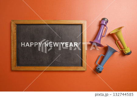 Greetings of Happy New Year on the blackboard with a plastic horn. Mockup or Copy space. Happy New Year concept or Celebration Greetings of Happy New Year on the blackboard with a plastic horn. Mockup or Copy space. Happy New Year concept or Celebration 132744585