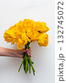 A boy stands indoors holding a large bouquet of yellow tulips, radiating happiness with a big smile on his face. Mother's Day and spring concept. 132745072