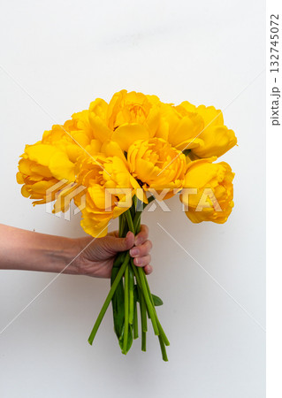 A boy stands indoors holding a large bouquet of yellow tulips, radiating happiness with a big smile on his face. Mother's Day and spring concept. 132745072