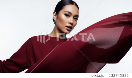 Confident fashion model with slicked back hair and makeup. Dynamic portrait with flowing red fabric on a white background 132745323