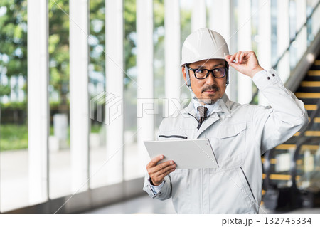 タブレットを操作する作業服の男性 132745334