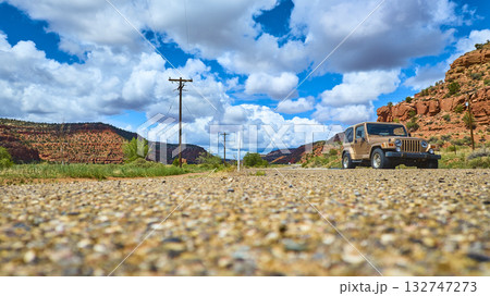 Jeep Wrangler on Desert Road with Red Rock Mesas and Dramatic Clouds Ground Level 132747273