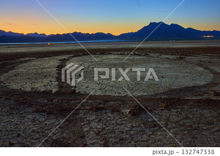 Cracked Dry Lake Bed With Tire Tracks And Mountains At Golden Hour Cracked Dry Lake Bed With Tire Tracks And Mountains At Golden Hour 132747338