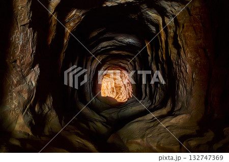 Hand Carved Rock Tunnel Interior with Sunlit Exit and Textured Walls Hand Carved Rock Tunnel Interior with Sunlit Exit and Textured Walls 132747369