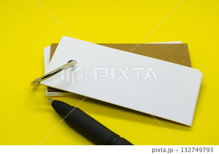 White banner shape notepad with customizable space for text on yellow cover background and a pen.. White banner shape notepad with customizable space for text on yellow cover background and a pen.. 132749793