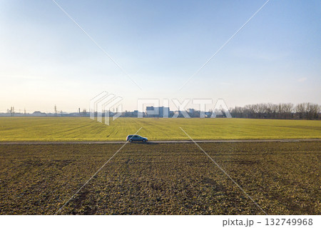 Aerial view of car driving by straight ground road through green fields on sunny blue sky copy space background. Drone photography. 132749968