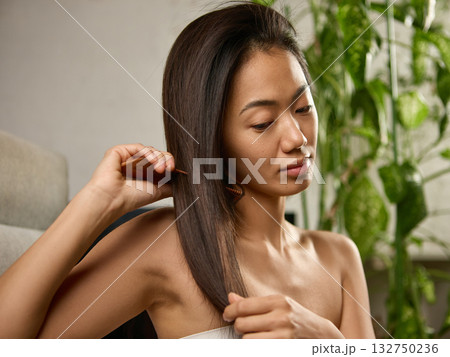 Young woman brushing long hair with peaceful focus in morning light 132750236