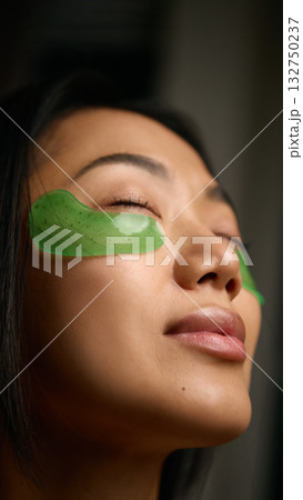 Woman relaxing with green under-eye patches enjoying quiet skincare moment 132750237