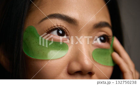 Closeup of female face with green eye patches showing hydration and care 132750238