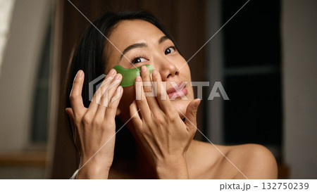 Woman applying green eye patches with calm expression and natural glow 132750239