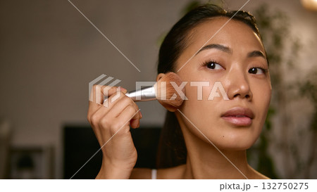 Woman applying blush with brush focusing on natural glow and tone Woman applying blush with brush focusing on natural glow and tone 132750275