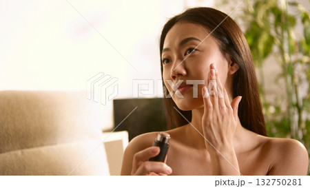 Woman applying serum on cheek with gentle thoughtful touch Woman applying serum on cheek with gentle thoughtful touch 132750281