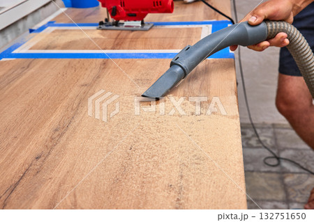 Worker man vacuums new kitchen after cutting hole for the sink in the kitchen countertops Worker man vacuums new kitchen after cutting hole for the sink in the kitchen countertops 132751650
