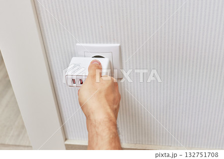 male hand insert a plug of the phone charger into socket at home 132751708