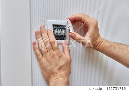 male hands of electrician installing white two-key electric light switch at home. Replacing. 132751716