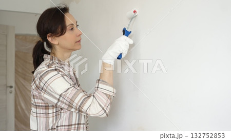 Woman wearing protective gloves painting white wall with small paint roller, updating interior and giving room clean, modern look during home renovation project Woman wearing protective gloves painting white wall with small paint roller, updating interior and giving room clean, modern look during home renovation project 132752853