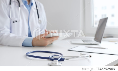 Closeup of blue stethoscope is lying on the table near female doctor reviewing prescription on digital tablet, representing digital healthcare workflow in contemporary medical setting. Medicine Closeup of blue stethoscope is lying on the table near female doctor reviewing prescription on digital tablet, representing digital healthcare workflow in contemporary medical setting. Medicine 132752903