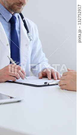 Unknown male doctor taking notes while listening to a female patient explaining her symptoms during a medical consultation in the clinic office. Medicine concept 132752917