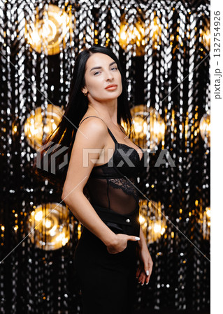 Young beautiful smiling brunette female in trendy evening clothes. Sexy carefree woman posing near shine wall in studio in a circle of light.Fashionable model with bright makeup 132754926