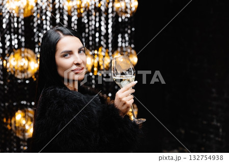 Young happy woman in trendy evening fur coat looking at camera and smiling with glass of champagne 132754938