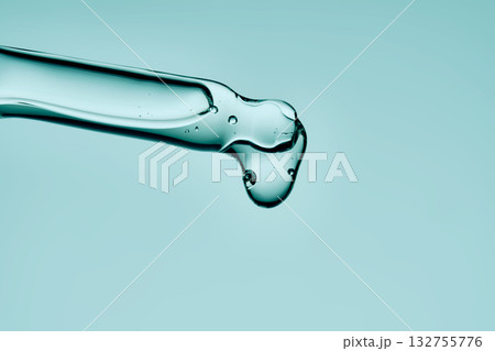 A drop of serum drips from a pipette on a delicate green background. A drop of serum drips from a pipette on a delicate green background. 132755776