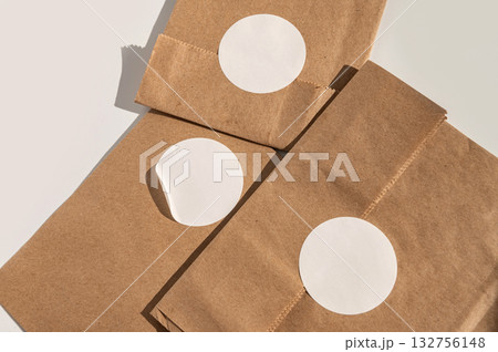 Brown paper bags with blank round white stickers on minimalist background Brown paper bags with blank round white stickers on minimalist background 132756148