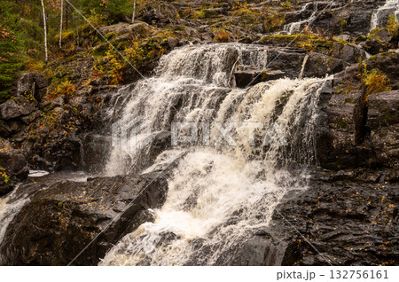 Cascading waterfall over rocky terrain in autumn forest scenery 132756161