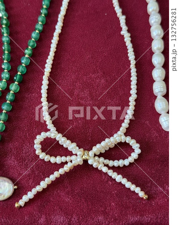 Pearl jewelry display with a creative bow shape on rich red velvet background 132756281