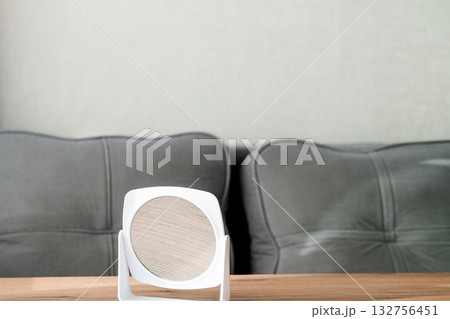 A white round plastic makeup mirror stands on a wooden table against the background of a sofa A white round plastic makeup mirror stands on a wooden table against the background of a sofa 132756451
