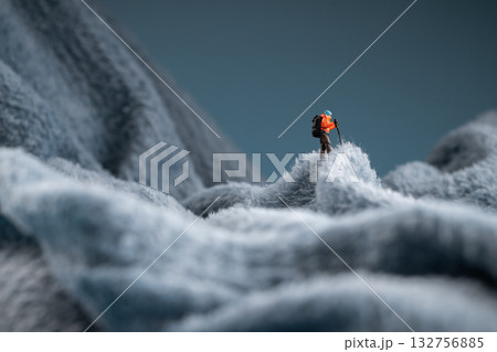 A miniature mountain climber figurine on a fuzzy fleece lining resembling a snow-covered surface, with a blurred background of a mountain or ice wall A miniature mountain climber figurine on a fuzzy fleece lining resembling a snow-covered surface, with a blurred background of a mountain or ice wall 132756885